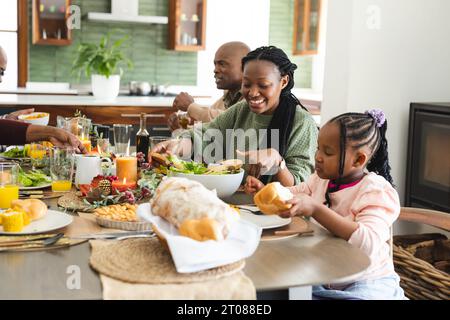 Glückliche afroamerikanische Mutter serviert Essen für Tochter beim Thanksgiving-Dinner Stockfoto