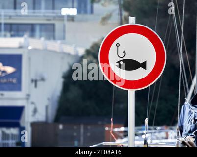 Schild mit einem Angelhaken und einem Fisch in einem roten Kreis, das darauf hinweist, dass das Fischen im Hafen verboten ist Stockfoto