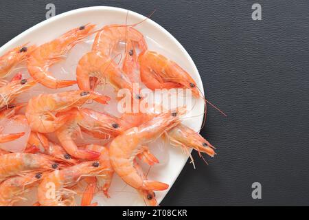 Frisch gekühlte Garnelen auf einer weißen Platte mit Eis auf grauem Hintergrund. Gekochte Garnelen auf einem Teller mit Eis, Draufsicht. Meeresfrüchte auf zerstoßenem Eis, gesundes Essen Stockfoto