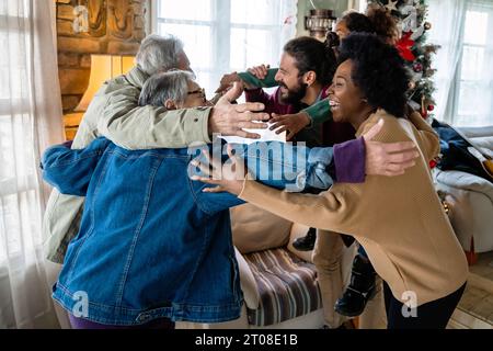 Aufgeregte multiethnische Familie begrüßt Großeltern am ersten Weihnachtsfeiertag. Eine glückliche Familie für mehrere Generationen Stockfoto
