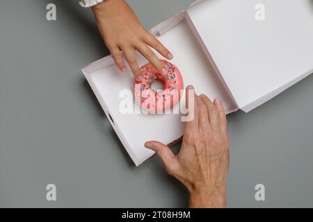 Farbenfroher rosafarbener Donut und menschliche Hände aus nächster Nähe an Bord, Blick von oben Stockfoto