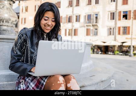 Ein Mädchen im Teenageralter benutzt ihren Laptop, während er im Stadtzentrum sitzt Stockfoto