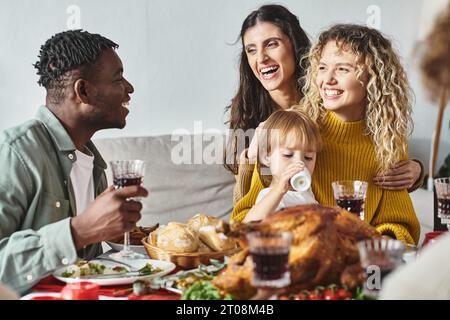 Fröhliches lgbt-Paar umgeben von Verwandten, die ihre Tochter in Händen halten, Weihnachtsfeier Stockfoto