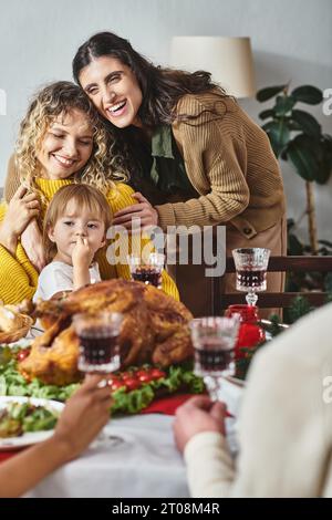 Fröhliches lgbt-Paar mit ihrer Tochter in den Händen und lächelnd fröhlich am Weihnachtstisch Stockfoto