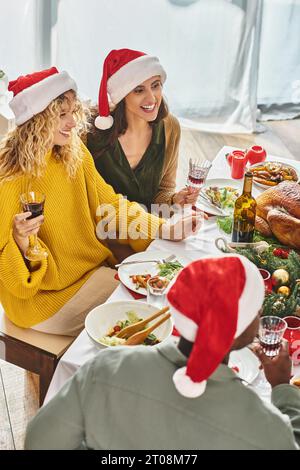 Fröhliches lgbt-Paar in Santa hat lächelnd und feiert Weihnachten mit ihren multiethnischen Verwandten Stockfoto