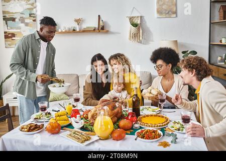 Fröhlicher afroamerikanischer Mann, der am Thanksgiving-Tag an Freunden und Verwandten eine Mahlzeit serviert Stockfoto