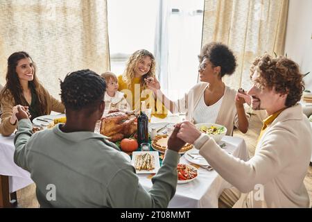 Fröhliche multirassische Freunde und Familie, die Hände halten und am Thanksgiving-Tisch beten, türkei-Tag Stockfoto