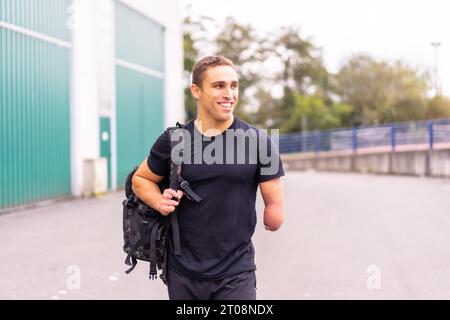 Glücklicher und junger Athlet mit einem Arm amputiert, der im Fitnessstudio ankommt Stockfoto