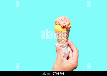 Eiskegel in der Hand vor blauem Hintergrund. Weibliche Hand, die Eiskegel hält. Vanileis Stockfoto