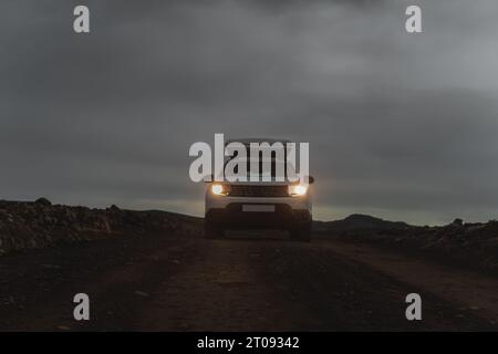 Dacia Duster 4x4 mit einem Dachzelt im Gelände in Landmannalaugar in Island. Frontaufnahme mit eingeschalteten Scheinwerfern und Schotter im Vordergrund. Schuss jus Stockfoto