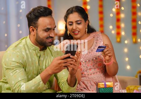 Glückliches aufgeregtes indisches junges Paar, das während der Diwali-Festivalfeier online mit Kreditkarte auf dem Handy kauft - Konzept des Erfolgs Stockfoto