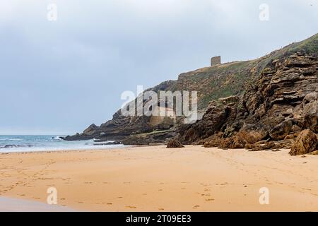 Malerischer Blick auf den grünen Berg mit der antiken Eremitage auf den Felsen nahe der Sandküste und dem schaumigen Ozean in Ermita de Santa Justa in Kantabrien, Spanien Stockfoto