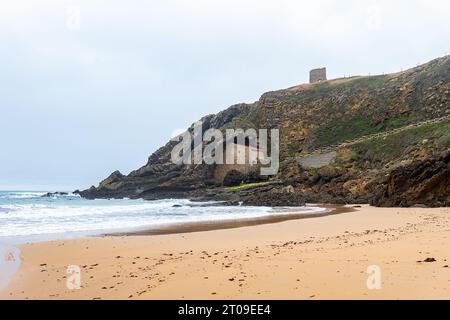 Malerischer Blick auf den grünen Berg mit der antiken Eremitage auf den Felsen nahe der Sandküste und dem schaumigen Ozean in Ermita de Santa Justa in Kantabrien, Spanien Stockfoto