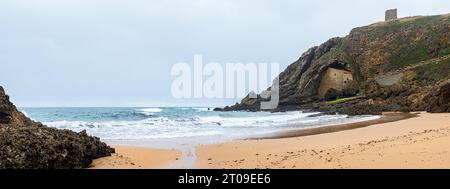 Malerischer Blick auf den grünen Berg mit der antiken Eremitage auf den Felsen nahe der Sandküste und dem schaumigen Ozean in Ermita de Santa Justa in Kantabrien, Spanien Stockfoto