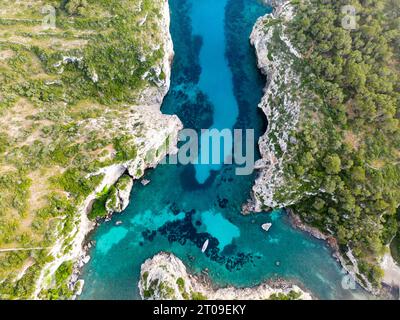 Blick von oben auf das transparente türkisfarbene Wasser des Meeres auf Menorca mit schwimmendem Segelboot an der Oberfläche Stockfoto