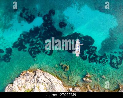 Blick von oben auf das transparente türkisfarbene Wasser des Meeres auf Menorca mit schwimmendem Segelboot an der Oberfläche Stockfoto