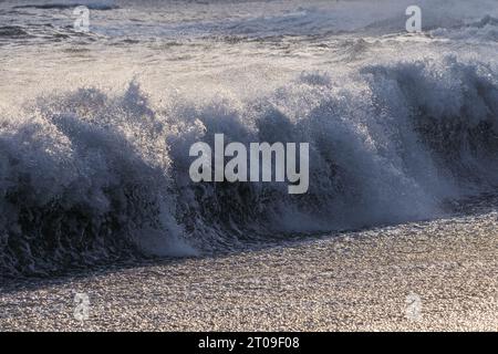 Mächtige, schaumige Meereswellen, die über der Wasseroberfläche vor dem bewölkten blauen Himmel am Strand von Reynisfjara Rollen und plätschern Stockfoto