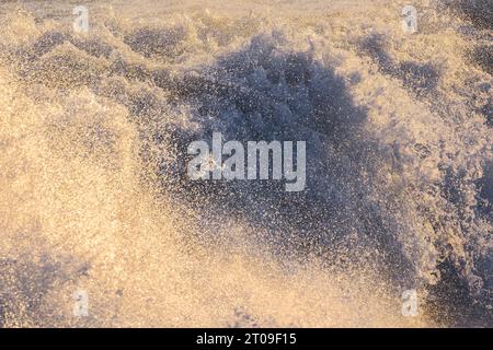 Mächtige, schaumige Meereswellen, die über der Wasseroberfläche vor dem bewölkten blauen Himmel am Strand von Reynisfjara Rollen und plätschern Stockfoto