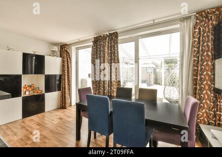 Das Innere des Esszimmers mit Tisch und Stühlen ist neben einem großen hellen Fenster in einem modernen Apartment angeordnet Stockfoto