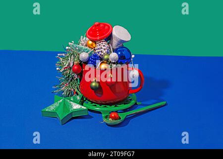 Weihnachtstisch mit verschiedenen bunten Ornamenten in rotem Topf auf blauem und grünem Hintergrund Stockfoto