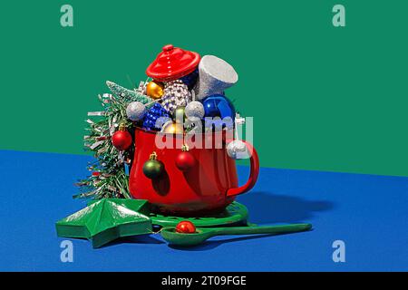 Weihnachtstisch mit verschiedenen bunten Ornamenten in rotem Topf auf blauem und grünem Hintergrund Stockfoto