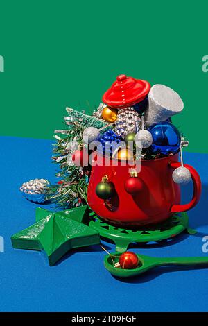 Hoher Winkel der Weihnachtstisch-Einstellung mit verschiedenen bunten Ornamenten in rotem Topf auf blauem und grünem Hintergrund Stockfoto