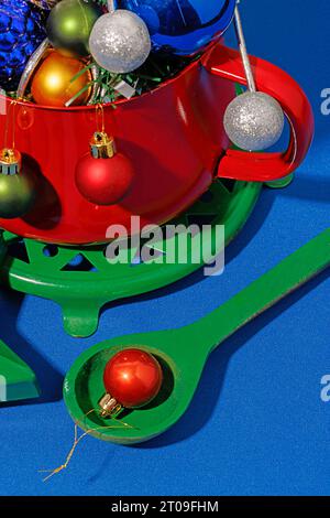 Hoher Winkel der Weihnachtstisch-Einstellung mit verschiedenen bunten Ornamenten in rotem Topf auf blauem Hintergrund Stockfoto