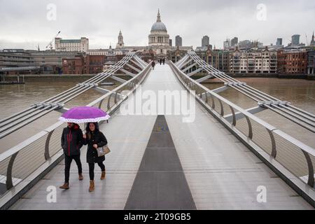 Aktenfoto vom 2/2021 von zwei Menschen, die unter einem Schirm untergebracht sind, als sie eine fast verlassene Millennium Bridge in der Nähe der St Paul's Cathedral im Zentrum Londons überqueren. Die Millennium Bridge über die Themse soll für drei Wochen wegen dringender Instandhaltungsarbeiten geschlossen werden. Die Fußgängerbrücke, die bei ihrer Eröffnung 2001 als „wackelige Brücke“ bezeichnet wurde, ist nicht gefährlich, aber eine Trennschicht unter dem Brückendeck hat begonnen, sich abzubauen und sie muss gründlich gereinigt werden, sagten die Eigentümer der City Bridge Foundation (CBF). Ausgabedatum: Donnerstag, 5. Oktober 2023. Stockfoto