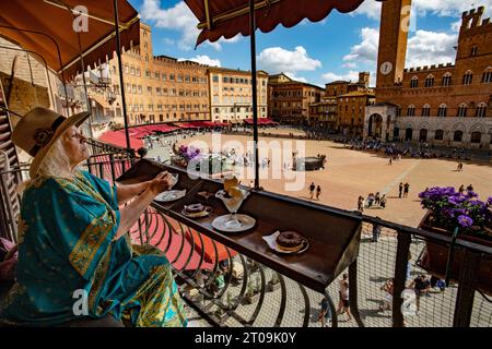 Siena Tuscany Italien September 2023 Model Released Woman genießt Eis und Kuchen mit Blick auf die Piazza del Campo und den Mangia-Turm (Torre de Stockfoto