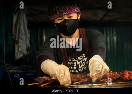 Ein Koch bereitet auf dem Nachtmarkt einen thailändischen Barbecue-Grill mit Fleischspießen zu. Die köstlichen Gerüche und Aromen ziehen hungrige Kunden auf dem Markt an. (Foto: Daniil Kiselev / SOPA Images/SIPA USA) Stockfoto