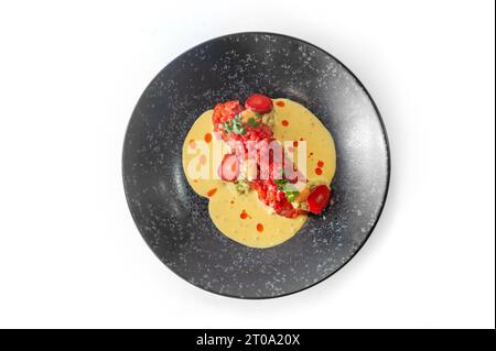 Lachstartar mit Erdbeeren, viel Soße und Chili-Fäden auf einer schwarzen Platte isoliert Stockfoto