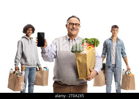 Lächelnder reifer Mann mit einem Smartphone, der vor jungen Männern mit Einkaufstaschen auf weißem Hintergrund steht Stockfoto