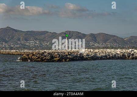 Ventura, CA, USA - 14. September 2023: Leuchtfeuer am Wave Mount Pier aus schweren Felsen am Eingang zum Hafen unter blauer Wolkenlandschaft. Blaues Meereswasser und Moun Stockfoto