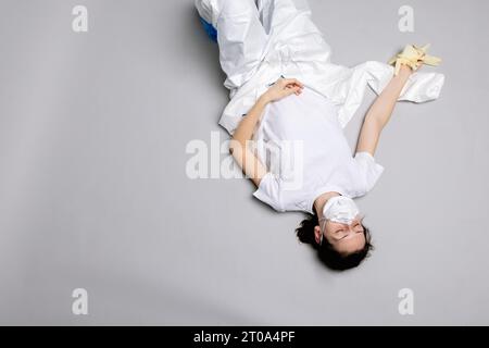 Müde Ärztin im Schutzanzug auf dem Boden, erschöpft Stockfoto