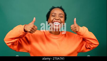 Die schöne schwarze Frau zeigt die Daumen nach oben, grüner Studiohintergrund Stockfoto