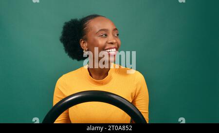 Schöne schwarze Frau fährt Auto lächelnd und sieht ruhig aus, grünes Studio Stockfoto