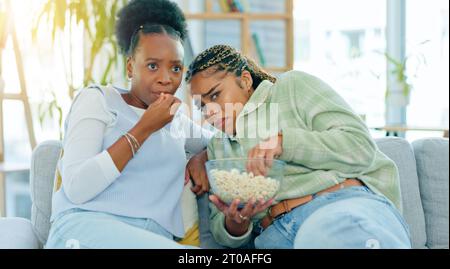 Schaurig, Film und Freunde auf Sofa im Wohnzimmer mit Popcorn, Snack oder köstlich im Haus. Schwarze Frauen, Menschen und zusammen, indem sie fernsehen, Horror oder Stockfoto