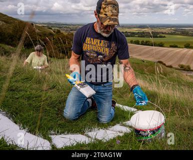 Volunters malen die Betonsteine, aus denen der lange Mann von Wilmington in East Sussex besteht. Ursprünglich wurde er in die Kreide des South Down gehauen. Stockfoto