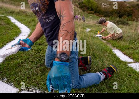 Volunters malen die Betonsteine, aus denen der lange Mann von Wilmington in East Sussex besteht. Ursprünglich wurde er in die Kreide des South Down gehauen. Stockfoto