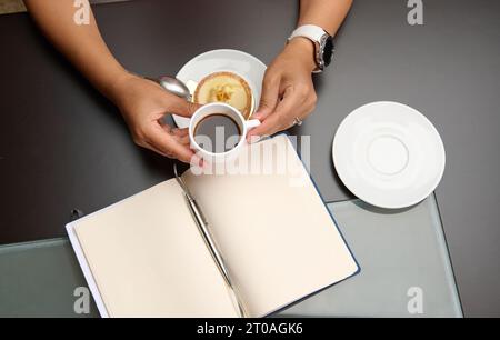 Blick von oben auf eine Frau, die eine Tasse Kaffee über einem Notizbuch hält, mit freiem Werbespot für Text Stockfoto