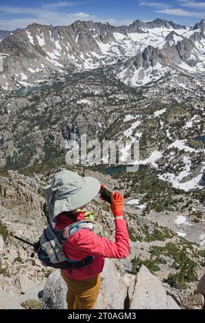 Eine Tageswandererin mit großem Sonnenhut macht ein Handyfoto vom Bergrücken der Sierra Nevada mit Blick auf das Becken des Lake Sabrina Stockfoto