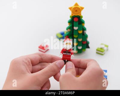 Tambow, Russische Föderation - 26. September 2023 Ein kleiner Junge, der eine Lego Santa Claus Minifigur in den Händen hält, über einem Weihnachtsbaum, umgeben von Chr Stockfoto