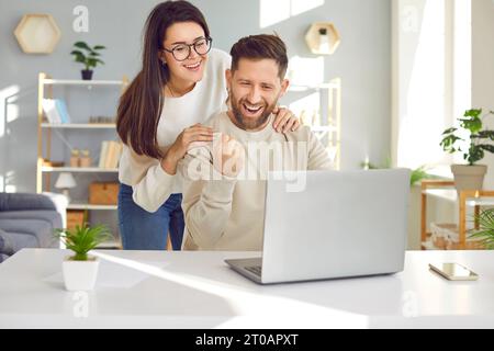 Fröhliches junges Paar, das zu Hause einen Laptop benutzt Stockfoto