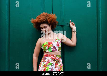 Schöne rothaarige Frau in farbenfrohem Kleid vor einer großen grünen Tür. Reisende Person. Stockfoto