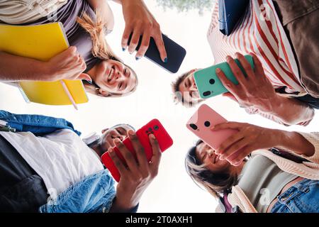 Low-angle-Ansicht einer multirassischen Gruppe junger erwachsener Freunde, die mit ihrer Handy-App Spaß und Lächeln haben. Porträt eines Schülers Hände, die ein Smartphone halten. Kollegen teilen sich mit Mobiltelefonen. Hochwertige Fotos Stockfoto