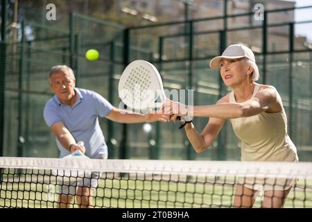 Motivierter Senior-Mann und -Frau spielen Padel mit seinem Teamkollegen vor Gericht Stockfoto