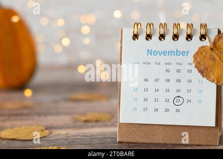 Thanksgiving Tag Datum 2023 im Kalender mit Herbstblättern markiert, und Kürbis auf Holztisch mit Bokeh Hintergrund. Nahaufnahme. Stockfoto