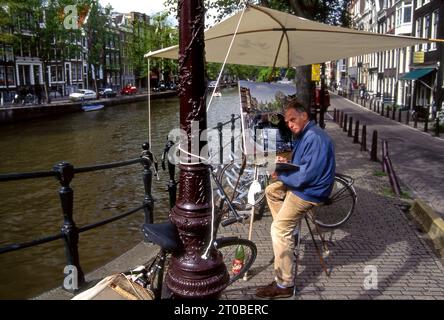 Künstler mit Leinwand auf Staffelei und Schirm, der ein Gemälde entlang der Kanäle in Amsterdam, Holland, macht Stockfoto