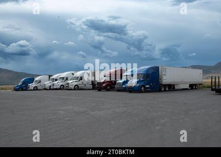 Sieben 18-Rad-Sattelzüge parkten in einer Resing-Station für Nahrung, Treibstoff oder Schlaf. Mit Gewitterwolken hinter den Fahrzeugen. Stockfoto