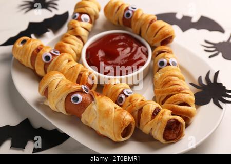 Teller mit leckeren Wurstmumien, Halloween-Deko und Ketchup auf weißem Tisch, Nahaufnahme Stockfoto